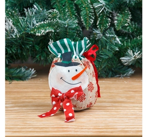 Close-up of burlap Christmas gift bag with snowman face and festive green pine background