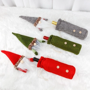 Three Christmas gnome wine bottle covers in red, green, and gray on a white plush rug