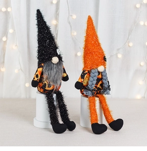Detail view of two plush Halloween gnomes with long legs on white pedestals and fairy lights
