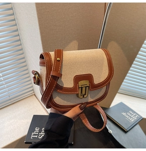 Detail of vintage saddle bag with brown leather trim, beige canvas, and bronze buckle clasp