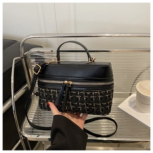 Detail of tweed and black leather stitching on a cylindrical crossbody bag with gold hardware