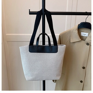 Detail of minimalist canvas tote bag with black leather trim and woven shoulder strap
