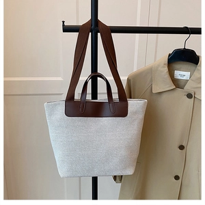 Detail of minimalist cream canvas tote bag with brown leather trim on a metal stand