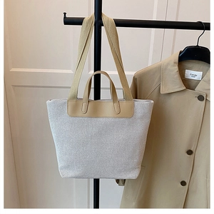 Detail view of canvas tote bag showing khaki leather straps and textured beige fabric