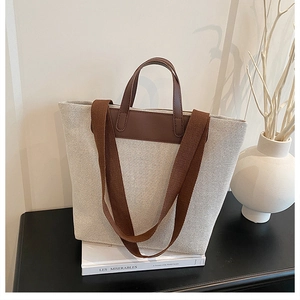 Close-up of beige canvas tote bag featuring brown leather accents and wide shoulder strap