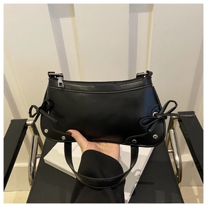 Detail of black leather baguette bag with side bow ties and silver rivet accents