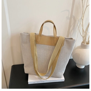 Close-up of canvas tote bag with leather trim and wide shoulder strap on minimal table