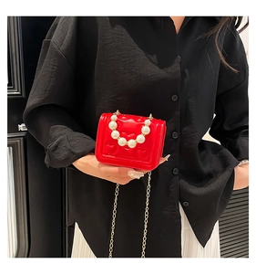 Detail of red heart-embossed mini bag featuring large pearl handle and gold chain strap