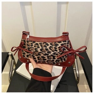 Detailed close-up of leopard print shoulder bag with red bow accents and silver metal studs