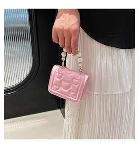 Detailed macro shot of pink heart-embossed mini bag with elegant pearl handle and gold chain