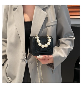 Detail of black heart-quilted leather mini bag with decorative pearl handle and gold chain
