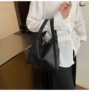 Detailed view of black litchi pattern leather tote bag with gold hardware worn by model