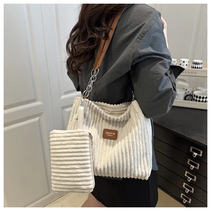 Detail of cream corduroy tote bag with brown leather patch and chain strap worn by model