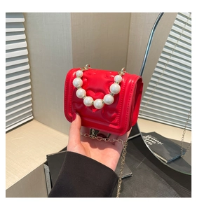 Detail of red heart-quilted mini bag featuring pearl handle and gold chain strap