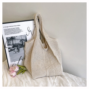 Détail d'un sac cabas en crochet blanc crème sur un décor de lit minimaliste