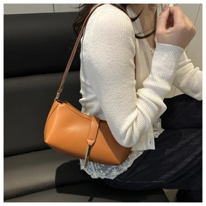 Close-up of a tan PU leather baguette bag with a sleek metal charm and matte texture