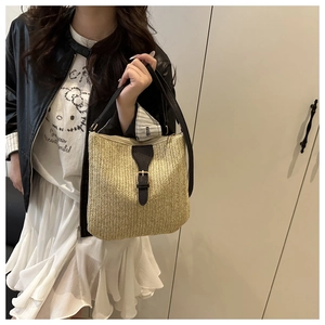 Detail of woven straw bucket bag with black leather trim and elegant gold buckle