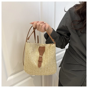 Close-up of woven straw bucket bag with brown leather trim and metal buckle detail