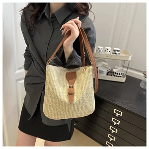 Close-up of woven straw bag featuring brown faux leather straps and buckle detail