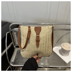 Detail of woven straw shoulder bag featuring brown leather strap and gold hardware