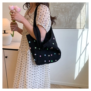 Detail of black crochet shoulder bag with colorful pearls and floral dress scene