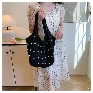 Close-up of black hollow knit shoulder bag with colorful pearls and hand-woven texture