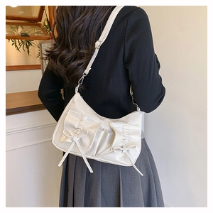 Détail d'un sac bandoulière blanc cassé avec nœuds et deux poches avant sur un mannequin
