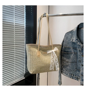 Detail of a large straw tote bag with leather handles and white lace bow decoration