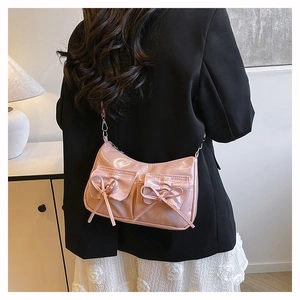 Sac à bandoulière rose brillant avec nœuds porté par un mannequin dans un intérieur
