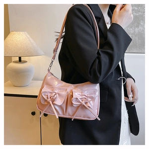 Gros plan du sac bandoulière rose en cuir verni avec nœuds 3D porté par un mannequin