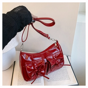 Gros plan du sac bandoulière en cuir verni rouge avec nœuds décoratifs et poches à rabat