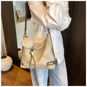 Detail of beige tote bag featuring a round coin purse charm and brown leather brand patch