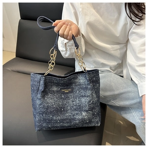 Détail d'un grand sac cabas en denim avec texture délavée et bandoulière chaîne dorée
