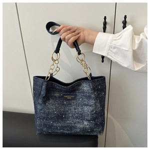 Détail du cabas en denim bleu avec poignées en chaîne dorée et écusson logo mode