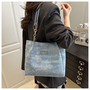 Détail du sac cabas en denim bleu clair avec logo en strass et bandoulière chaîne