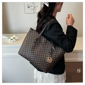 Detail of a coffee brown monogram tote bag featuring a gold M charm and thin leather handles