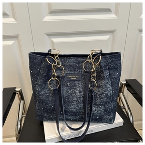 Détail d'un sac cabas en denim bleu avec chaîne dorée et poignée en cuir