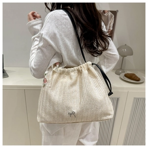 Detail of straw woven beach tote bag with floral embroidery and silver bow charm