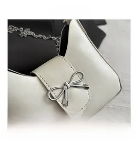Close-up of white leather baguette bag with silver bow hardware and metal chain