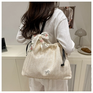 Detail of cream straw tote bag with delicate weaving, bow charm, and lace floral ribbon