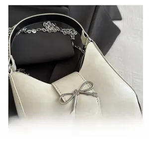 Detail of a creamy baguette bag with a silver bow buckle and elegant metal chain strap