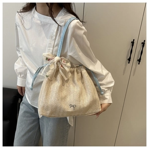 Detail of straw bucket bag with blue straps and embroidered lace bow decoration