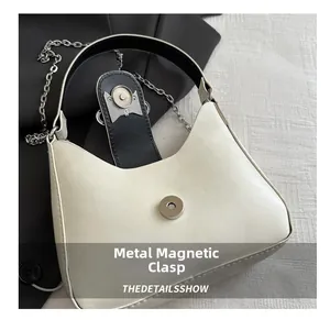 Detail of the high-quality metal magnetic clasp on a white crescent shoulder bag