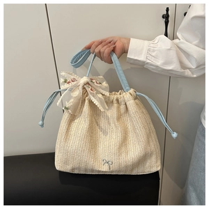 Close-up of woven straw tote bag with floral embroidery lace bow and blue leather straps