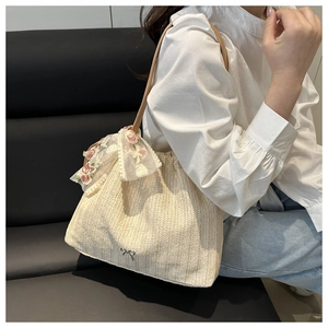 Close-up of beige woven tote bag featuring delicate lace ribbons and silver bow charm