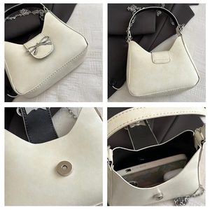 Detail views of cream baguette bag with silver bow accent, chain strap, and inner storage