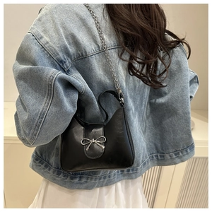 Detail of black faux leather baguette bag with silver bow accent and chain strap