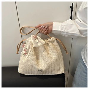 Detail of straw tote bag showing V-shaped weave, silver bow, and lace floral scarf