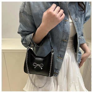 Close-up of black matte leather shoulder bag featuring silver bow hardware and chain strap