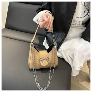 Close-up of khaki baguette bag with silver metallic bow and elegant chain strap